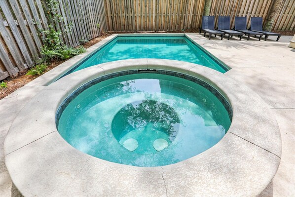 A swimming pool with a hot tub in the center, surrounded by a wooden fence and a bench area.