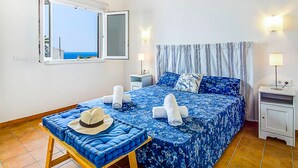 A bedroom with a large bed, a window with a view, a bedside table, and a nightstand. - VILLA FARO (Cap d´Artruix)
