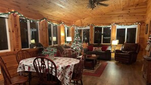 Interior acolhedor de uma cabana com uma mesa de jantar, cadeiras, um sofá e um pinheiro de Natal.