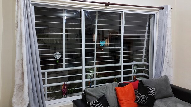 A living room with a large window, a grey sofa with patterned cushions, and a curtain with a floral pattern.