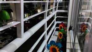 A balcony with white railings, a row of colorful sunflowers, and a view of parked cars and buildings in the background.