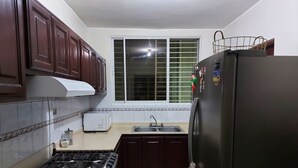 A compact kitchen with dark wooden cabinets, a gas stove, a refrigerator, and a window with blinds.