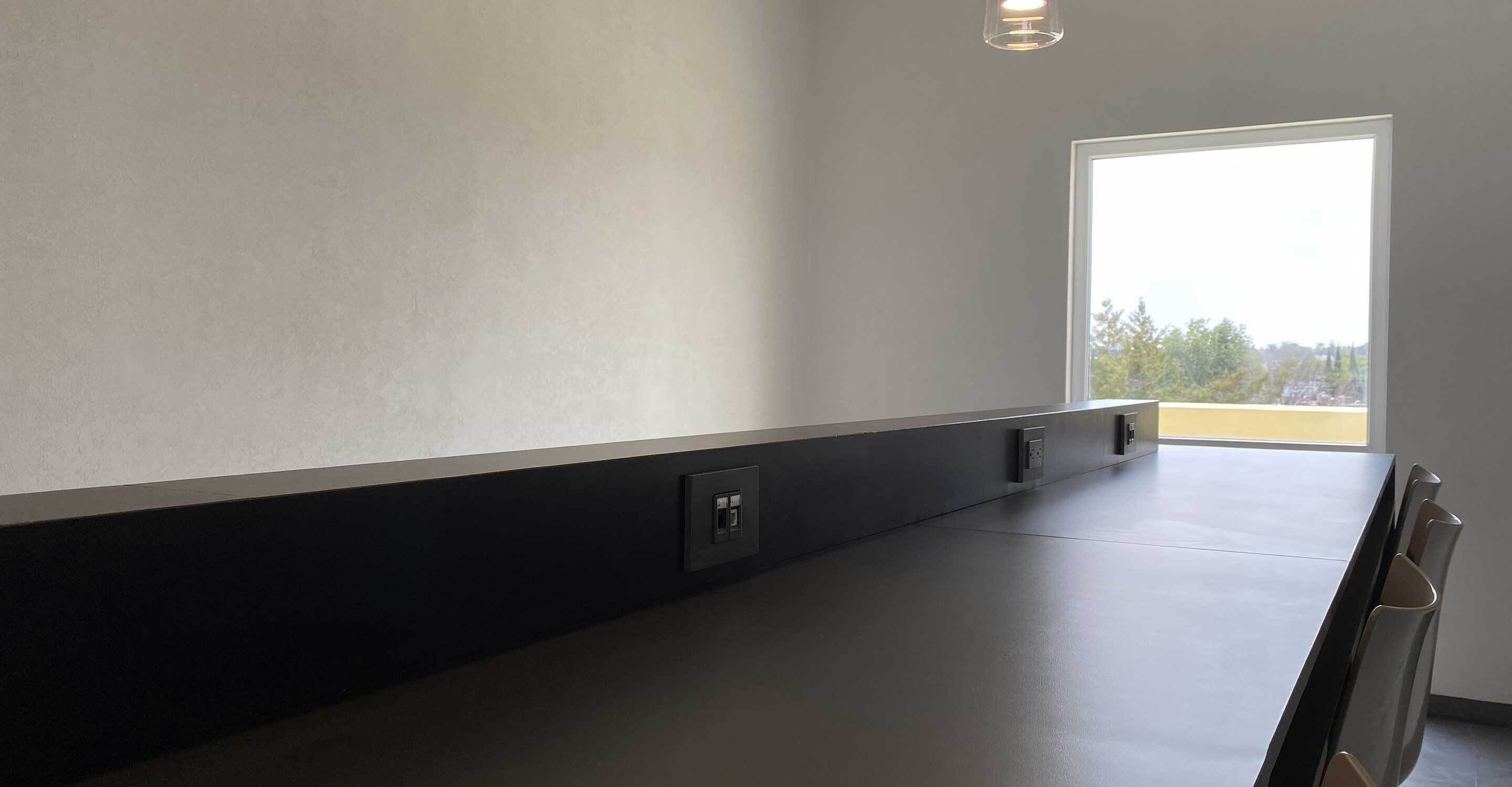 Una habitación moderna con un ventanal grande, una mesa oscura y una silla.