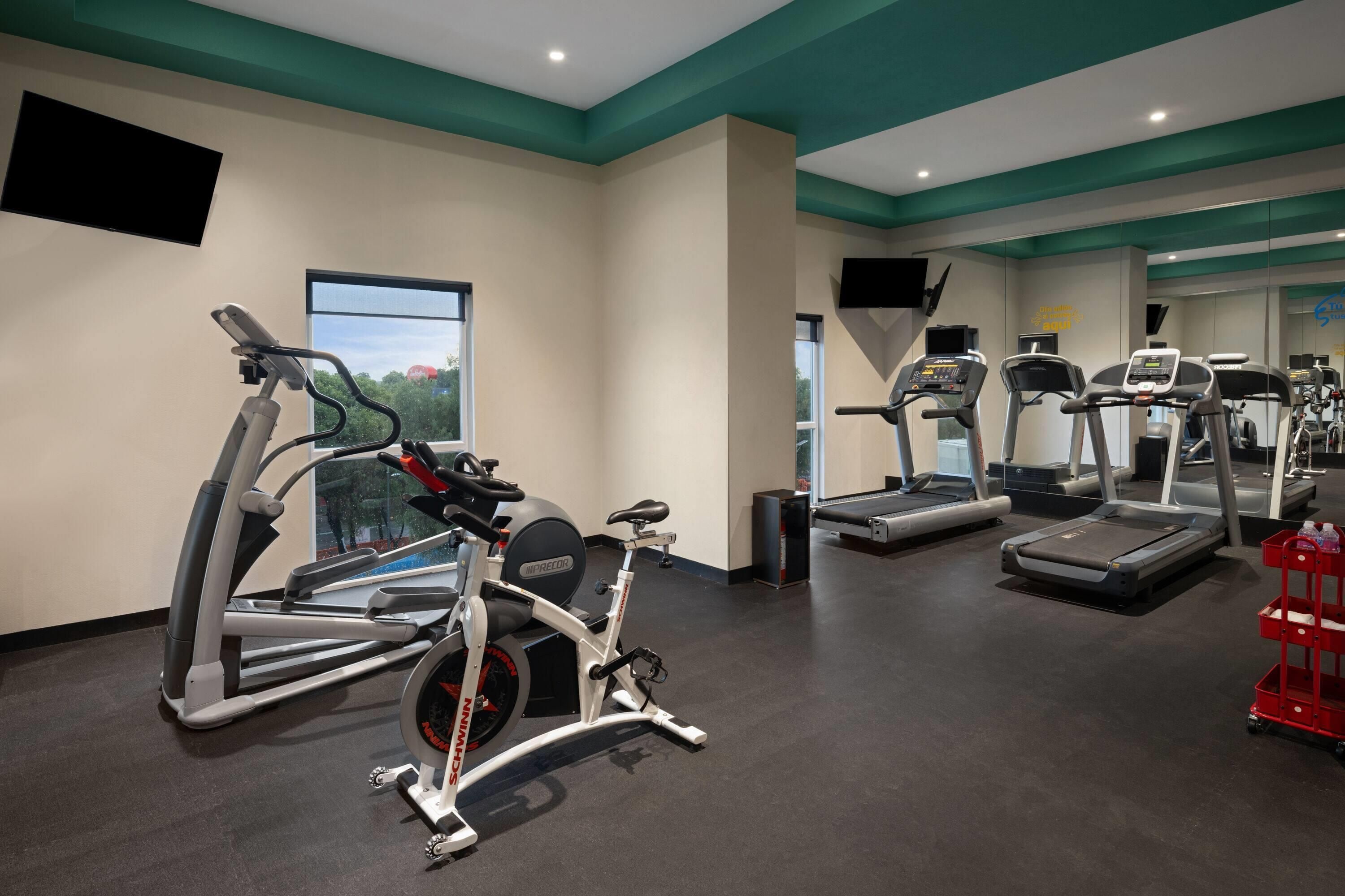 Une salle de sport équipée de divers appareils d’exercice, notamment des tapis de course, des vélos d’appartement et des appareils de musculation elliptique.