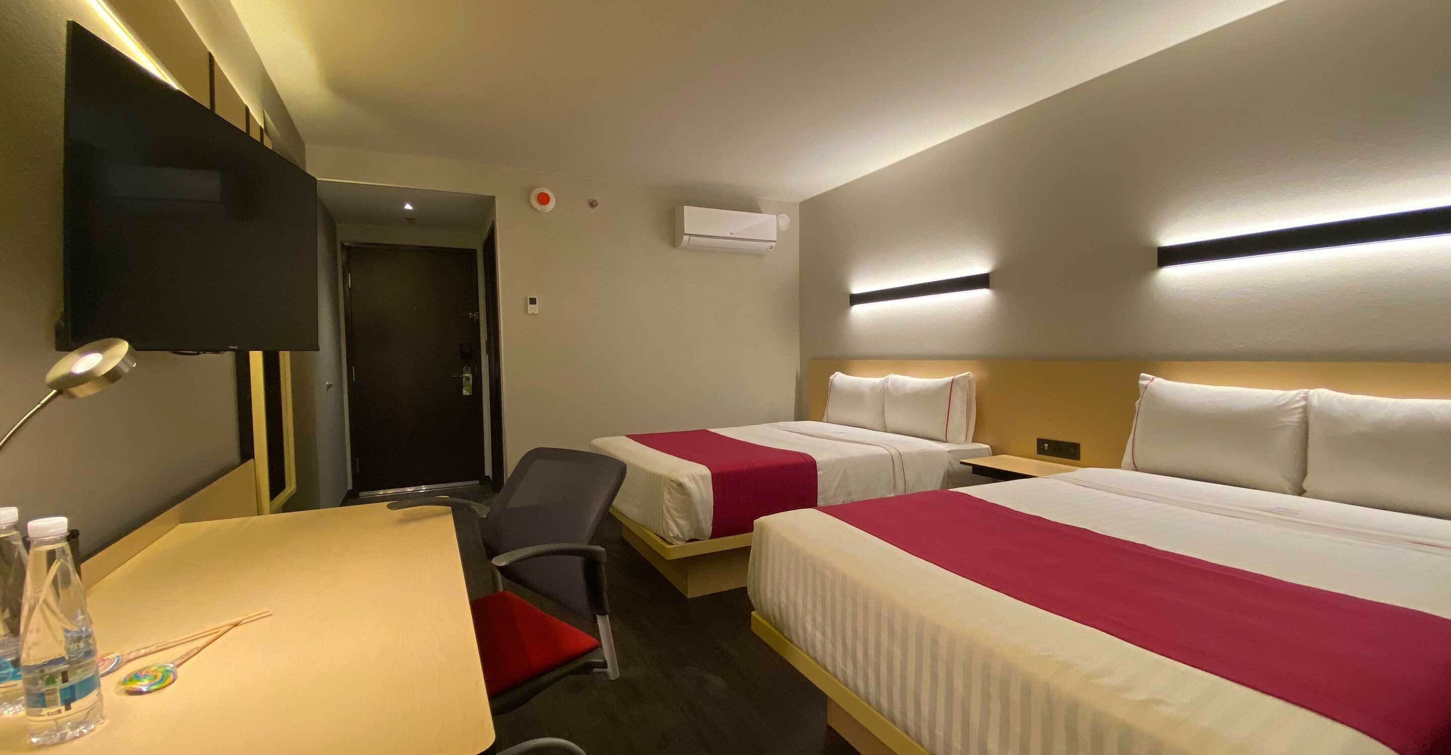 Habitación de hotel con dos camas, un escritorio, una silla, un televisor y un equipo de aire acondicionado.