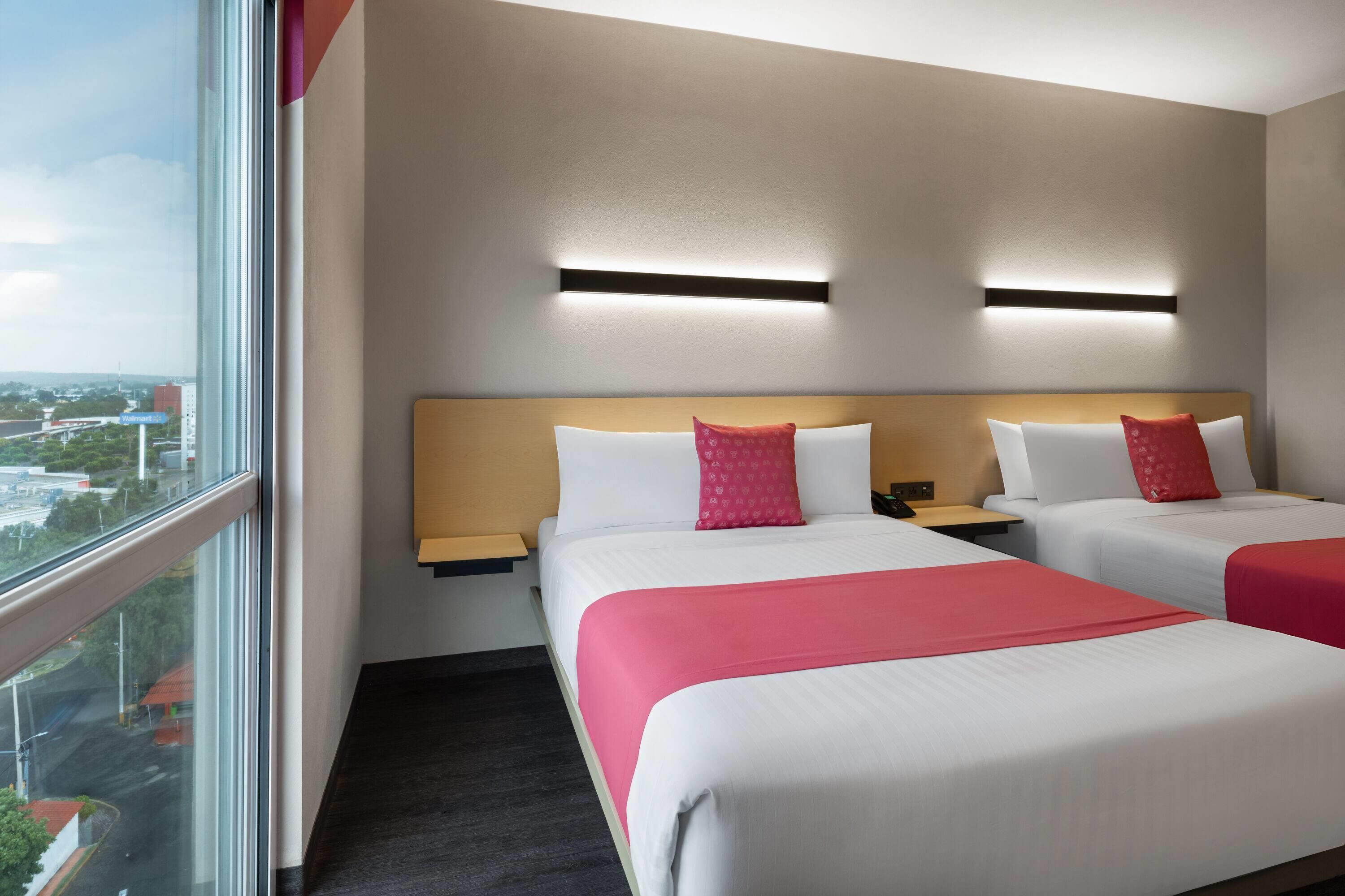 A hotel room with two beds, a large window, and a city view.