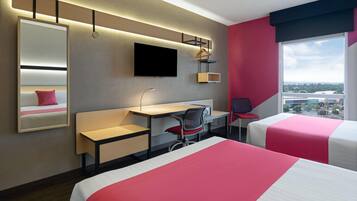 Habitación de hotel con cama, escritorio, silla, televisión y ventana con vista a la ciudad.