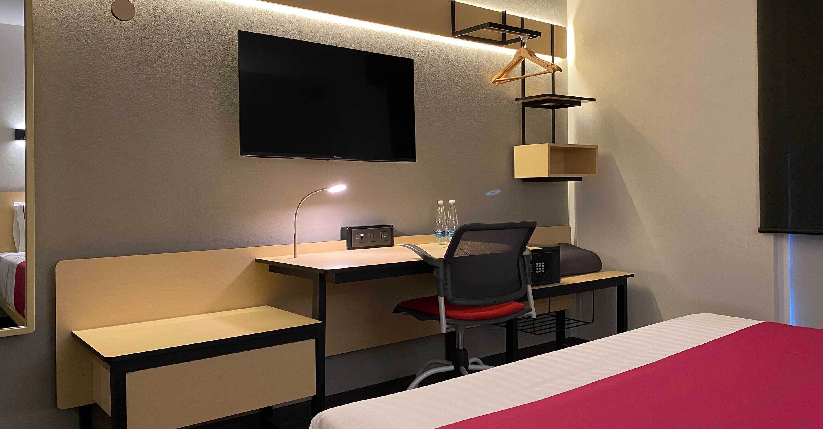 Hotelkamer met een bed, een bureau met stoel, een aan de muur bevestigde televisie en een hanglamp.