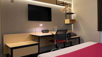 Hotelkamer met een bed, een bureau met stoel, een aan de muur bevestigde televisie en een hanglamp.