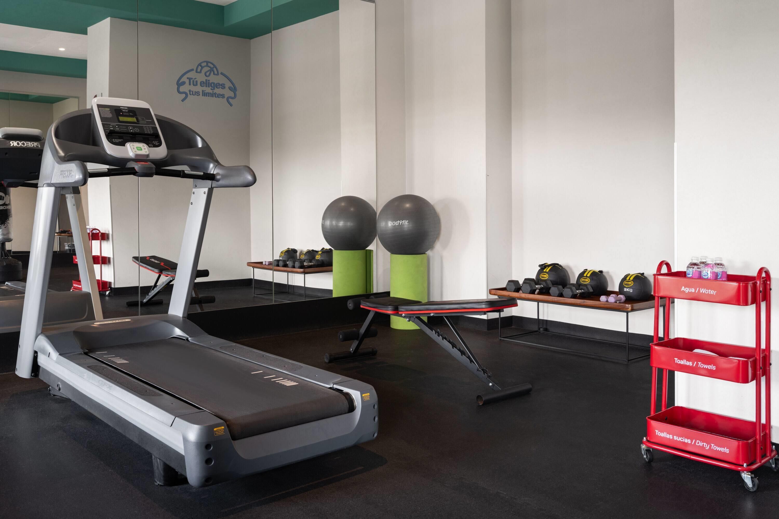 A gym with a treadmill, exercise balls, dumbbells, and a water cart.
