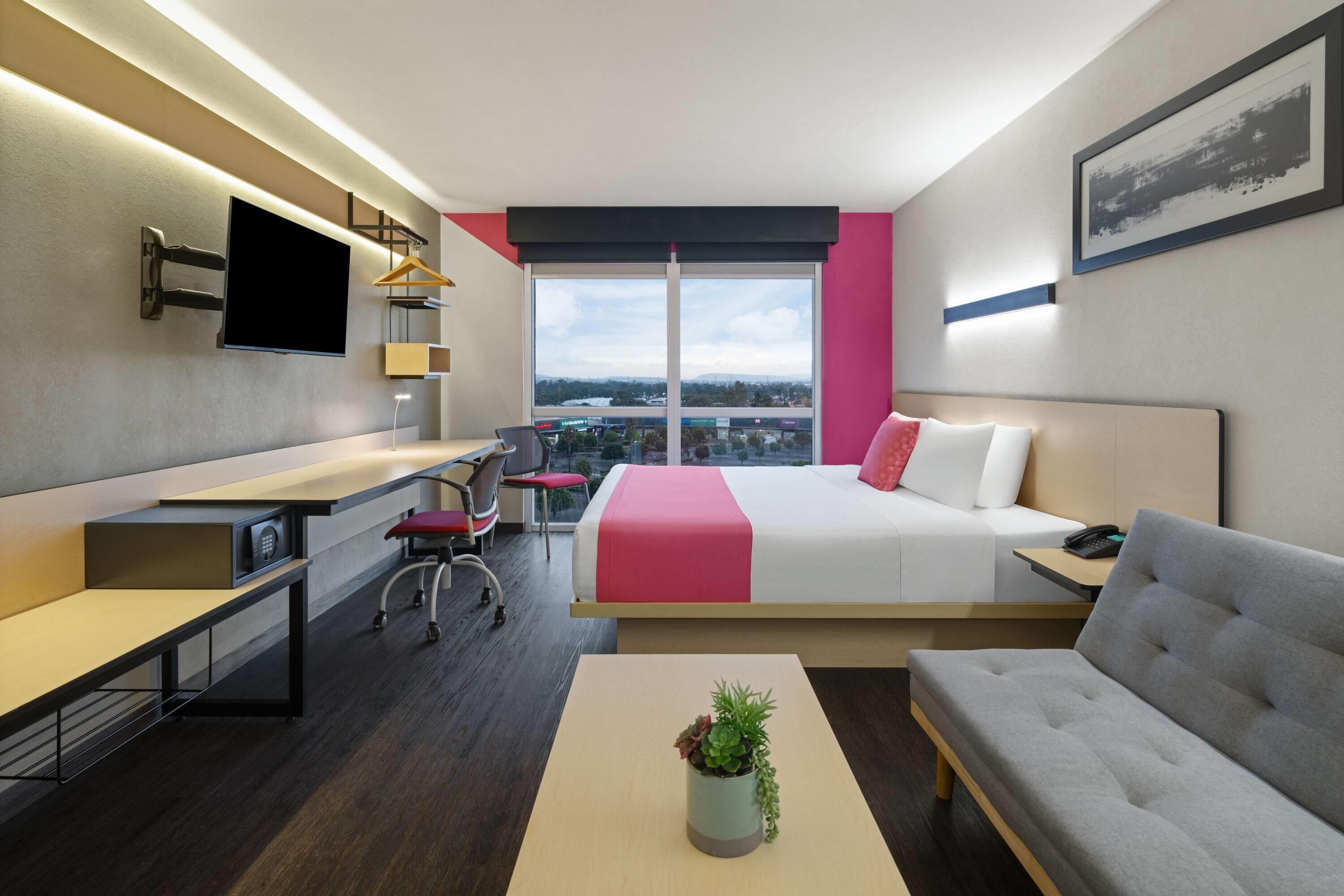 Een moderne hotelkamer met een bed, een bureau, een bank, een televisie en een raam met uitzicht op de stad.