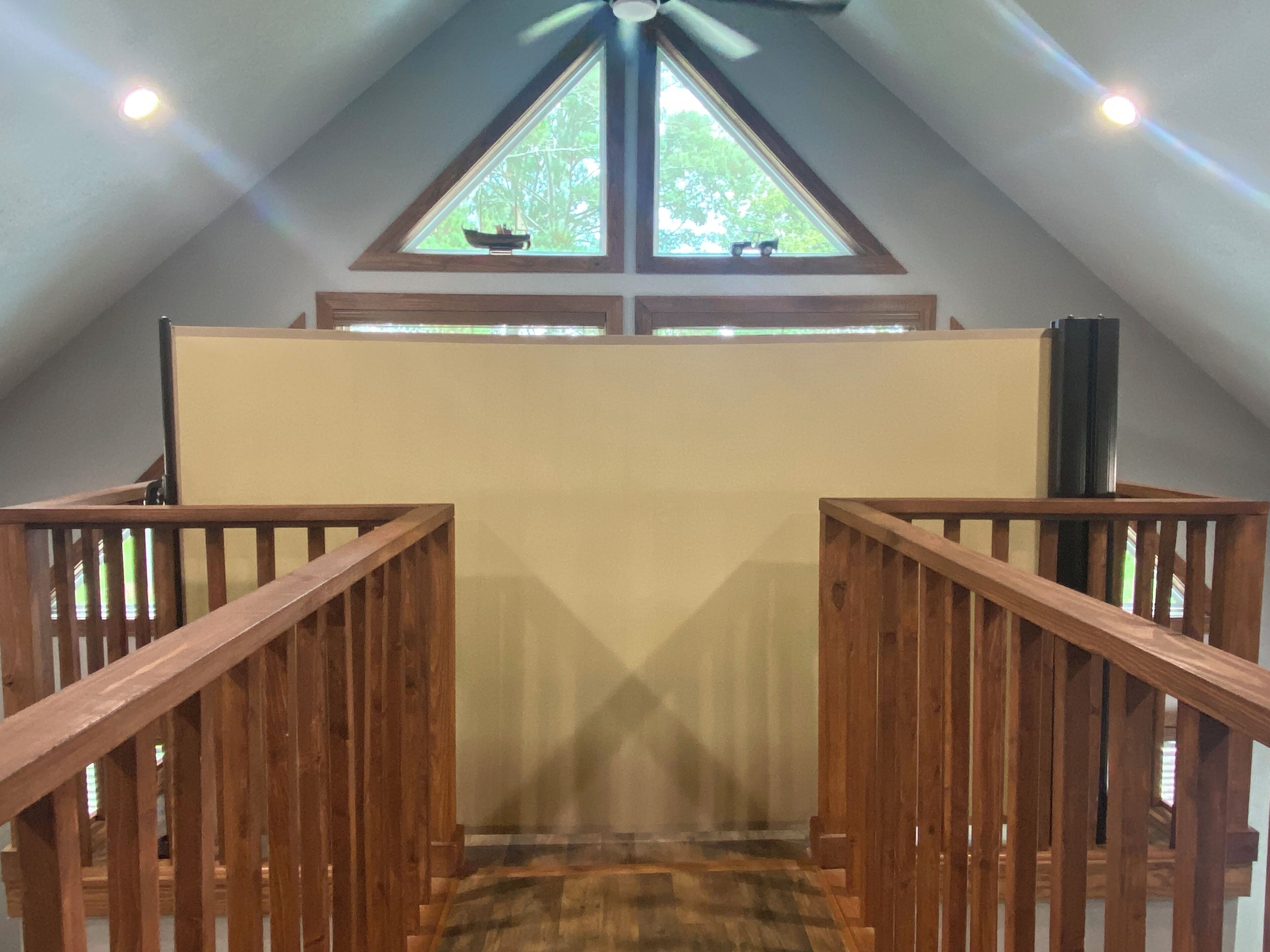 A view of a wooden staircase leading to a loft area with a sloped ceiling and a window with a view of trees.