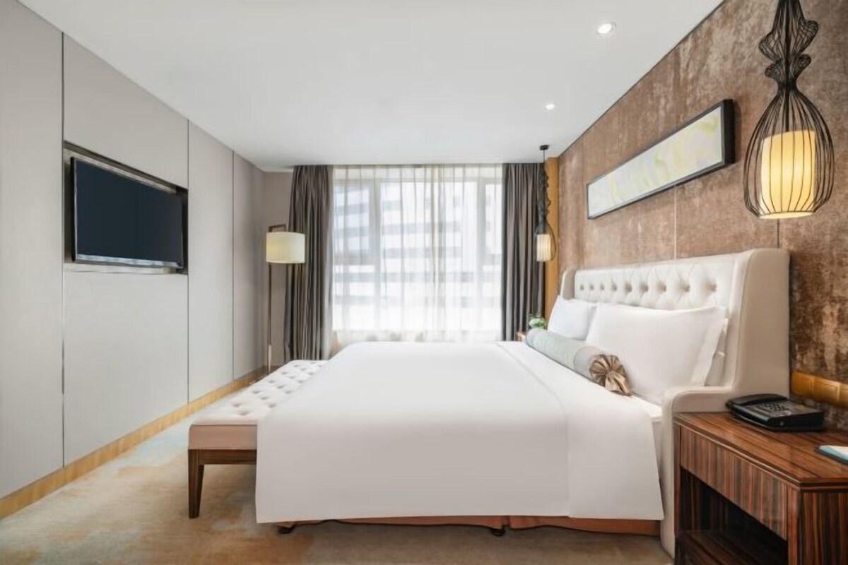 A hotel room with a large bed, a television, a bedside table, and a window with curtains.
