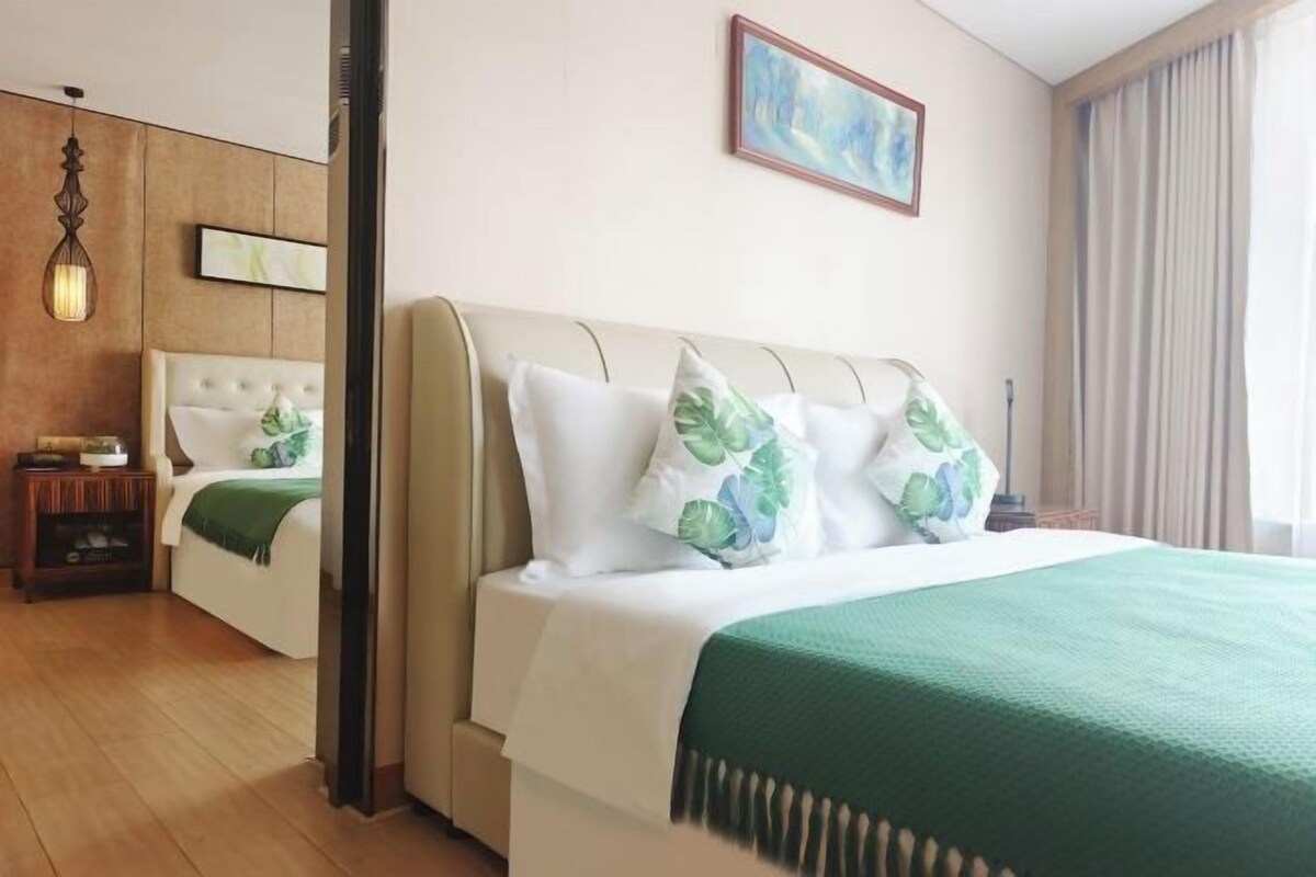 A hotel room with a bed, a nightstand, a lamp, a painting on the wall, and a window with curtains.