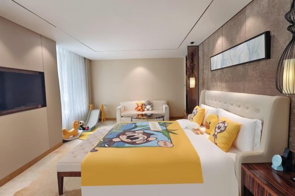 A hotel room with a bed, a sofa, a TV, and a wall-mounted artwork.