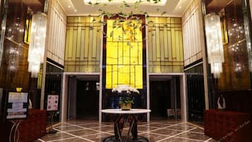 A lobby with a central column, chandeliers, a reception desk, and a tiled floor.