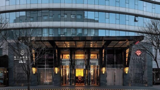 A modern hotel entrance with a curved facade, glass doors, and illuminated signage. - Beijing Minyoun Lia! by Minyoun Hotel (Wangfujing Commercial Street Dongdan Subway Station) (Beijing)