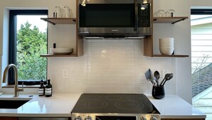 A modern kitchen with a built-in microwave, stove, and wooden cabinets. - Greenwood Getaway - Modern and New, Walk to Shops (Seattle)