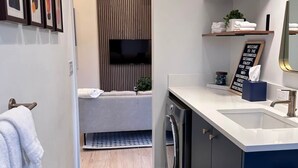 A modern bathroom with a built-in washing machine, a sink, and a towel rack. - Greenwood Getaway - Modern and New, Walk to Shops (Seattle)