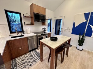 A modern kitchen with a built-in oven, microwave, and stainless steel dishwasher. There is a dining area with a table and chairs, and a potted plant.