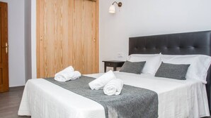 Ein ordentlich bezogenes Bett mit weißer und grauer Bettwäsche, ein dunkler Kopfteil und ein Holzschrank in einem Hotelzimmer.