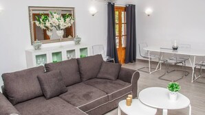 Ein modernes Wohnzimmer mit einem grauen Ecksofa, einem Essbereich mit weißem Tisch und Stühlen sowie einem großen Spiegel über einer Ablagetisch mit Dekoration.