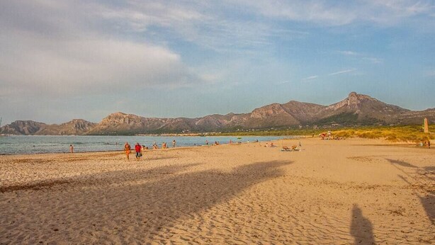 Ein Strand mit Spaziergängern, einem klaren Himmel und Bergen im Hintergrund.