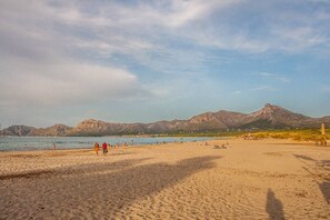 En strand med folk som promenerar, en klar himmel och berg i bakgrunden.