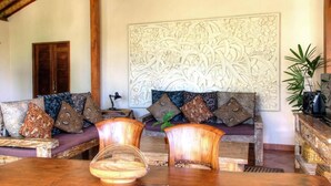 Un salon chaleureux avec un plafond en bois, un canapé agrémenté de coussins à motifs, un élément décoratif mural et une petite table sur laquelle est posé un bol.