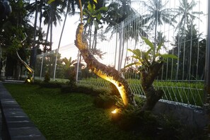A garden with a curved tree, a metal fence, and a grassy area. - Lily Lane Villas (Ubud)