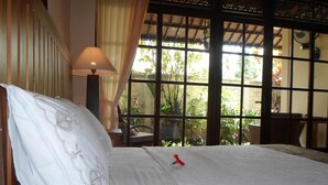 Une chambre d’hôtel avec un grand lit, une fenêtre donnant sur un espace verdoyant et une table avec une lampe.