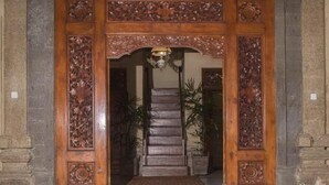 Une porte d’entrée en bois ornée de sculptures complexes, un escalier menant à l’intérieur et des plantes en pot.