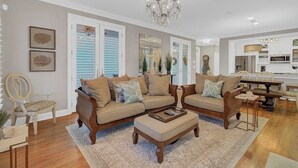 A spacious living room with a large chandelier, two sofas with matching cushions, a coffee table, and a dining area with a chandelier. - Award-Winning Resort Amenities | Grand Pavilion 67 (Isle of Palms)