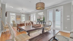 A dining room with a large wooden table, white upholstered chairs, and a chandelier. - Award-Winning Resort Amenities | Grand Pavilion 67 (Isle of Palms)