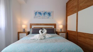 Een net opgemaakt bed met een blauw beddegoed met patroon, twee bedlampen, een houten hoofdbord en een wanddecoratie.