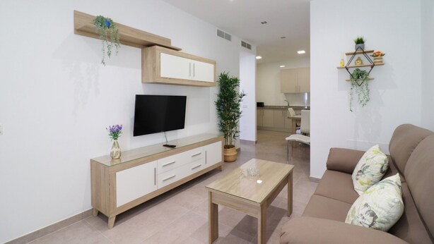 Een moderne woonkamer met een flatscreen-tv, een glazen salontafel, een bank en een eethoek op de achtergrond.