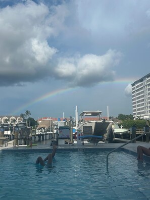 Piscina com uma pessoa na água, um barco atracado por perto e um edifício ao fundo.