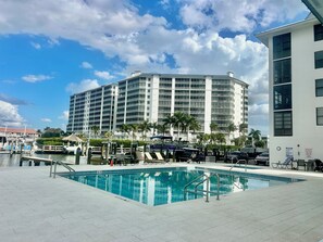A large hotel with a swimming pool, palm trees, and a clear sky.