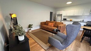 A modern living room with a sofa, armchair, and a small table with a bottle and glass. - 3 Bed Budget Brisbane Gem With Parking Near Gabba (Woolloongabba)
