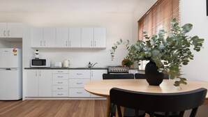 A modern kitchen with white cabinets, a microwave, a kettle, and a dining table with chairs. - 3 Bed Budget Brisbane Gem With Parking Near Gabba (Woolloongabba)