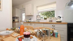 A kitchen with white cabinets, a wooden countertop, and a window. There is a table set with plates, glasses, and a bottle of orange juice. - Ground Floor At The Lawns - Lovely chic ground floor apartment (Filey)