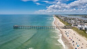 A pier extending into the ocean with a beach and buildings in the background. - Penthouse Ocean Front Resort  (Wrightsville Beach)