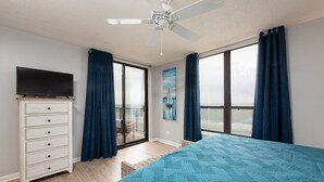 A bedroom with a bed, a dresser, a ceiling fan, and a view of the ocean through large windows. - Penthouse Ocean Front Resort  (Wrightsville Beach)