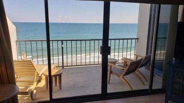 A balcony with a view of the sea, wooden furniture, and a glass door. - Penthouse Ocean Front Resort  (Wrightsville Beach)
