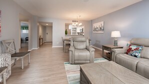 A spacious living room with a grey sofa, a leather armchair, and a dining area with a chandelier. - Penthouse Ocean Front Resort  (Wrightsville Beach)