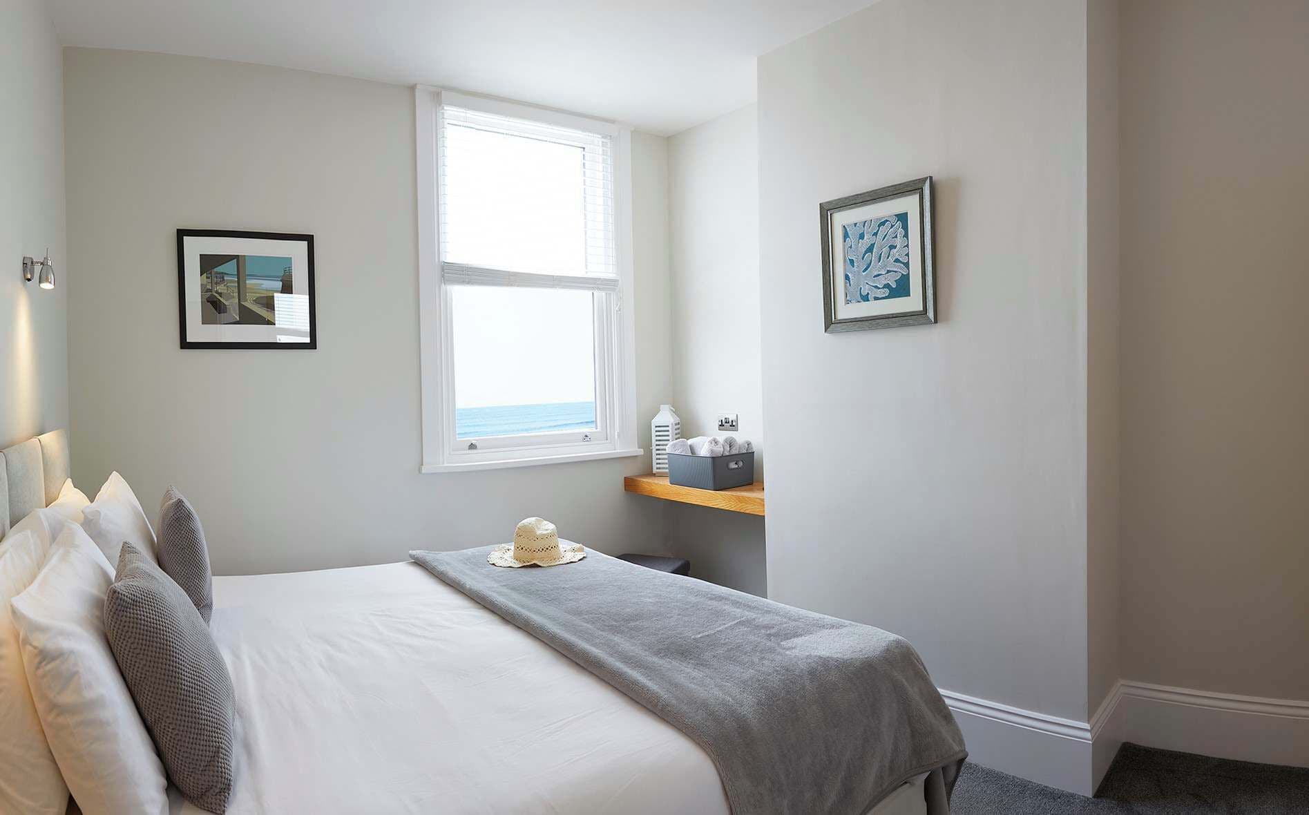 A bedroom with a bed, a window with a view, a bedside table with toiletries, and two framed pictures on the wall.