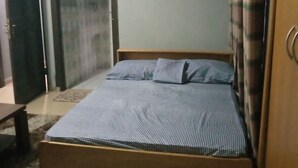 A bedroom with a wooden bed, a small table, and a door leading to another room. - Short Stay Apartment (Accra)