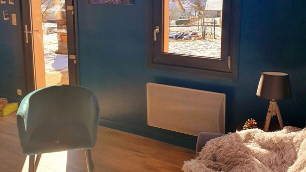 Une pièce avec une grande fenêtre, une chaise, une table, un radiateur et une lampe.