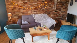 Un salon chaleureux avec un mur en bois, un canapé, deux fauteuils bleus, une table basse et un téléviseur.