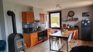 Une cuisine moderne avec des armoires en bois, un four encastré, un four à micro-ondes et une cuisinière noire. On y trouve également un coin repas avec une table et des chaises, ainsi qu’un réfrigérateur décoré d’aimants.